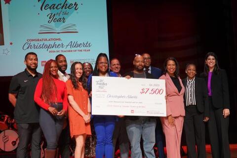 Christopher Alberts, Howard alum and a music educator at the School Without Walls High School, on stage and smiling as he receives D.C.'s 2026 Teacher of the Year award.